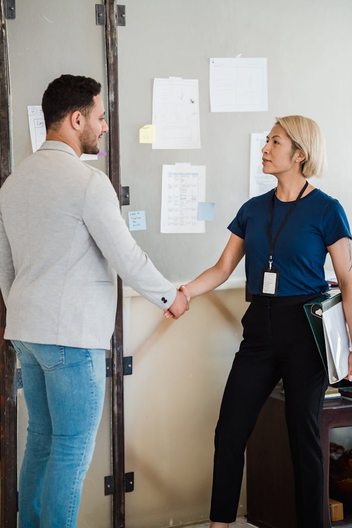 Two professionals shaking hands in an office setting, symbolizing collaboration.