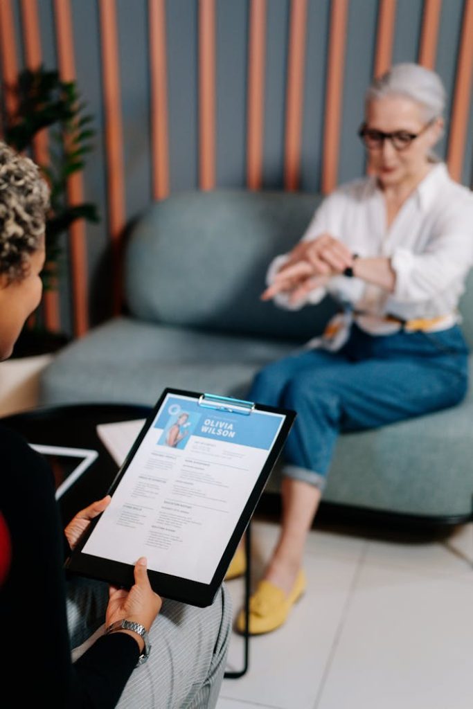 A senior woman being interviewed indoors with her resume displayed.